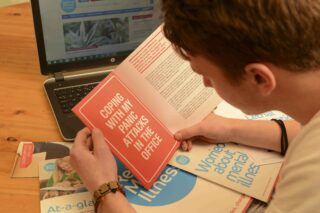 Man reading leaflet that says 'coping with my panic attacks in the office'