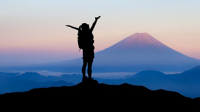 silhouette of a woman stood on top of a mountain with arms outstretched